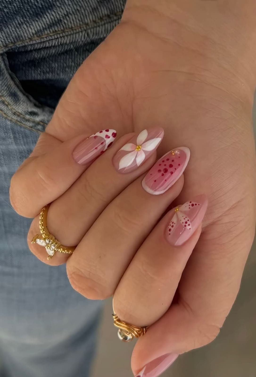 Uñas almendradas en rosa translúcido con una flor blanca pintada a mano y lunares granate